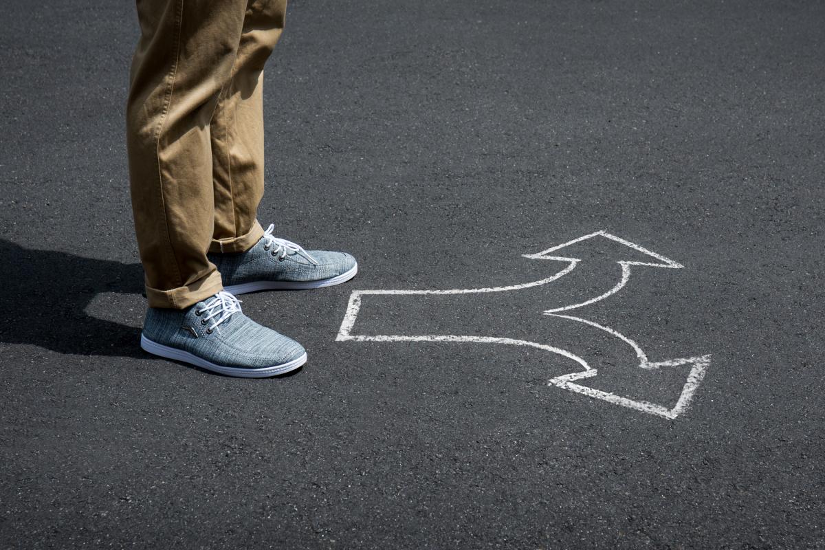 Young man standing on a street with arrow signs pointing in diff