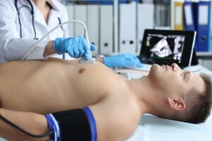 Doctor,Doing,Heart,Ultrasound,To,Young,Male,Patient,In,Clinic